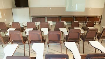 A classroom with rows of desks and chairs, a projector screen, and a television on a cabinet.