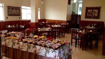 A buffet setup in a dining area with multiple tables and chairs, a floral tablecloth, and various food items displayed.