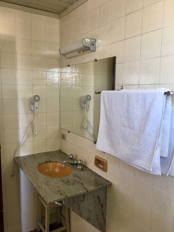 A bathroom with a marble sink, two hair dryers, a towel rack with a white towel, and a mirror.