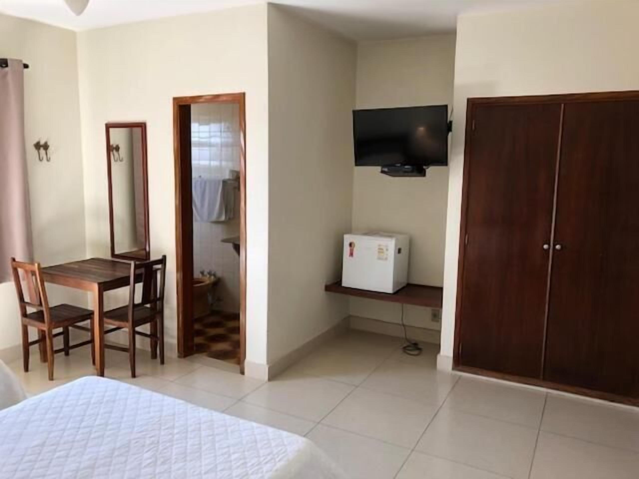Una habitación pequeña y limpia con cama, escritorio y silla, armario y un refrigerador pequeño.