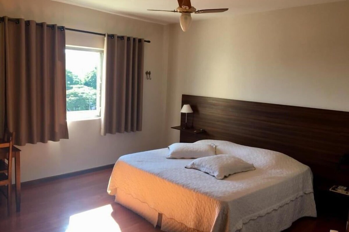 A bedroom with a bed, curtains, a ceiling fan, and a nightstand with a lamp.