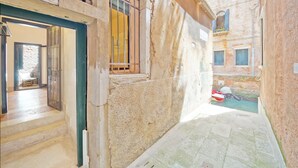 A narrow alleyway with a stone wall and a wooden door leading to a room.