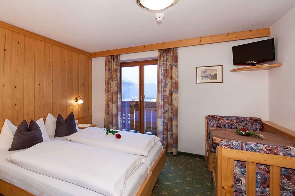 A wooden-paneled room with a bed, bedside tables, a TV, and a balcony with curtains.