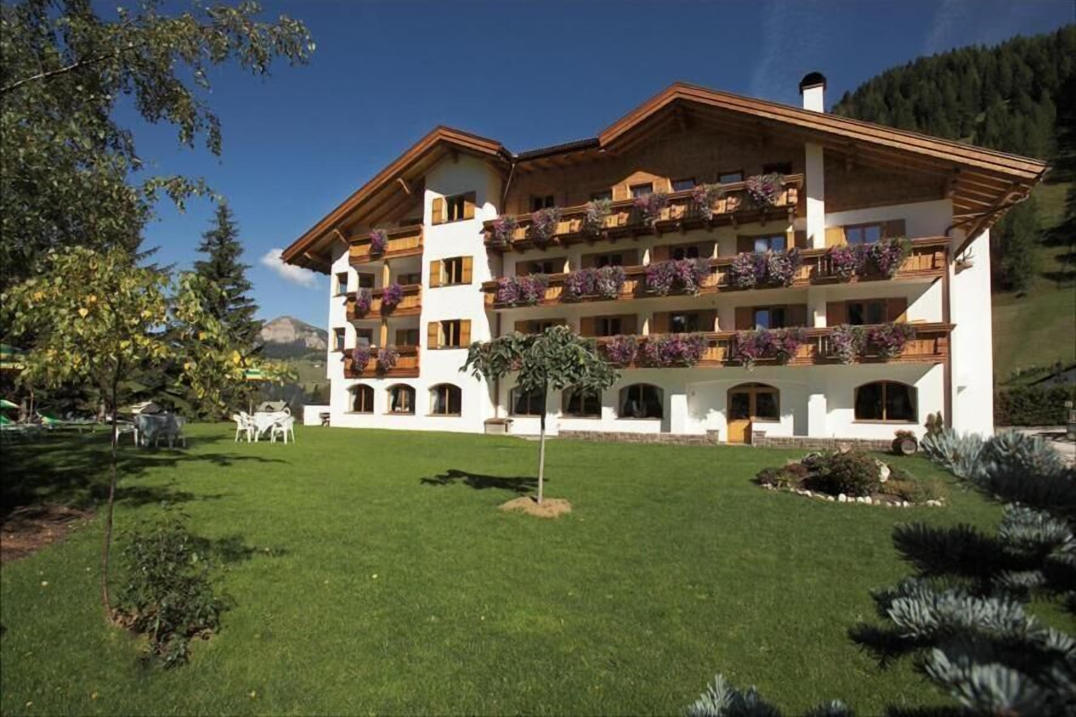 Een hotel met meerdere verdiepingen, balkons, een verzorgd gazon en een bergachtige achtergrond.