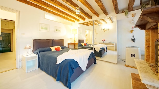 Quarto com teto de madeira, cama com cobertor branco, mesa de cabeceira com luminária e espelho na parede.