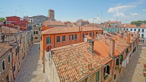 Rua estreita com edifícios de telhado em terracota, uma torre imponente e um céu azul claro.