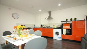 Una cocina moderna con armarios color naranja, una mesa de comedor blanca y un reloj en la pared.