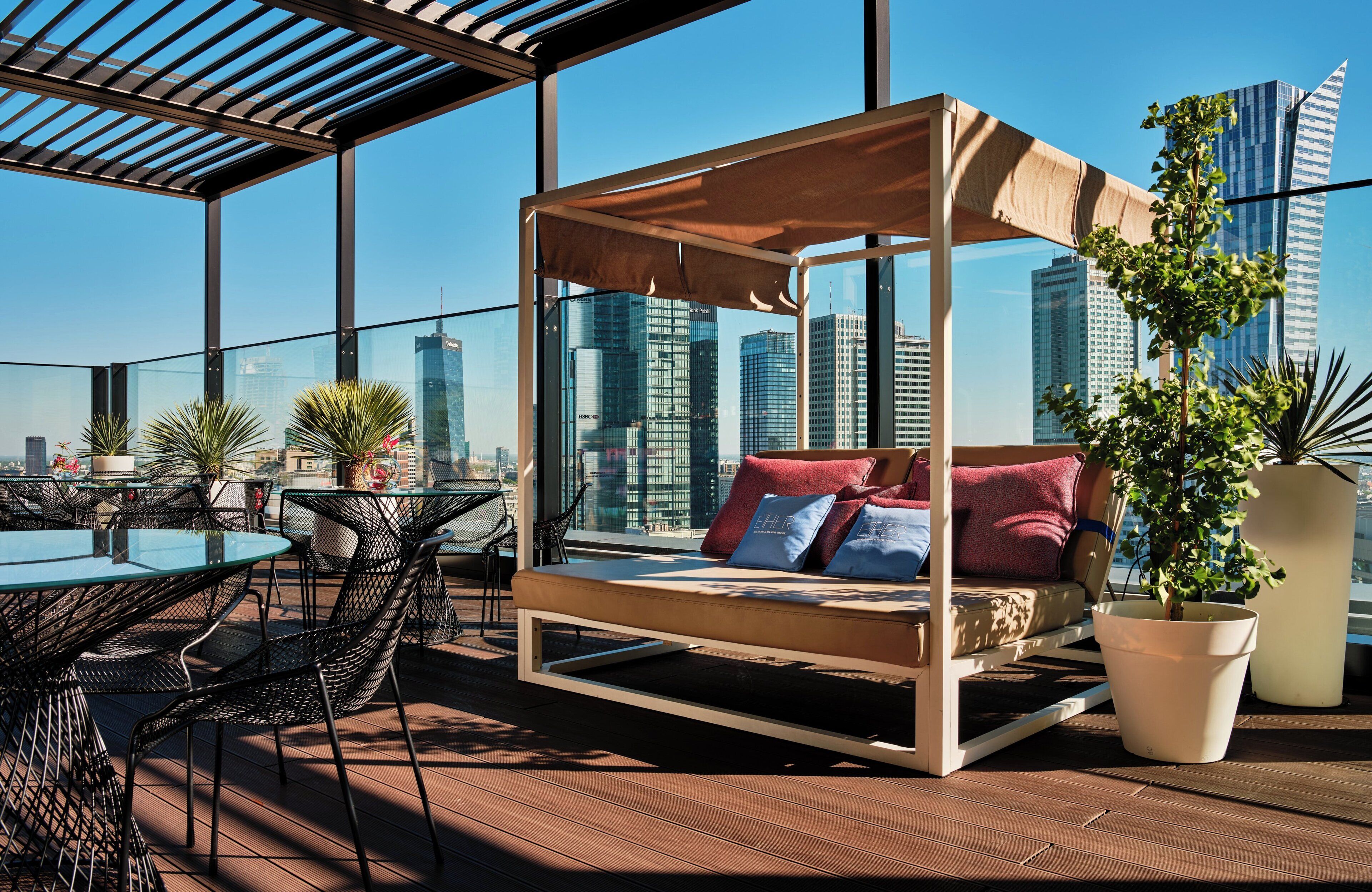 A rooftop lounge with a glass-enclosed bed, outdoor dining area, and city views.