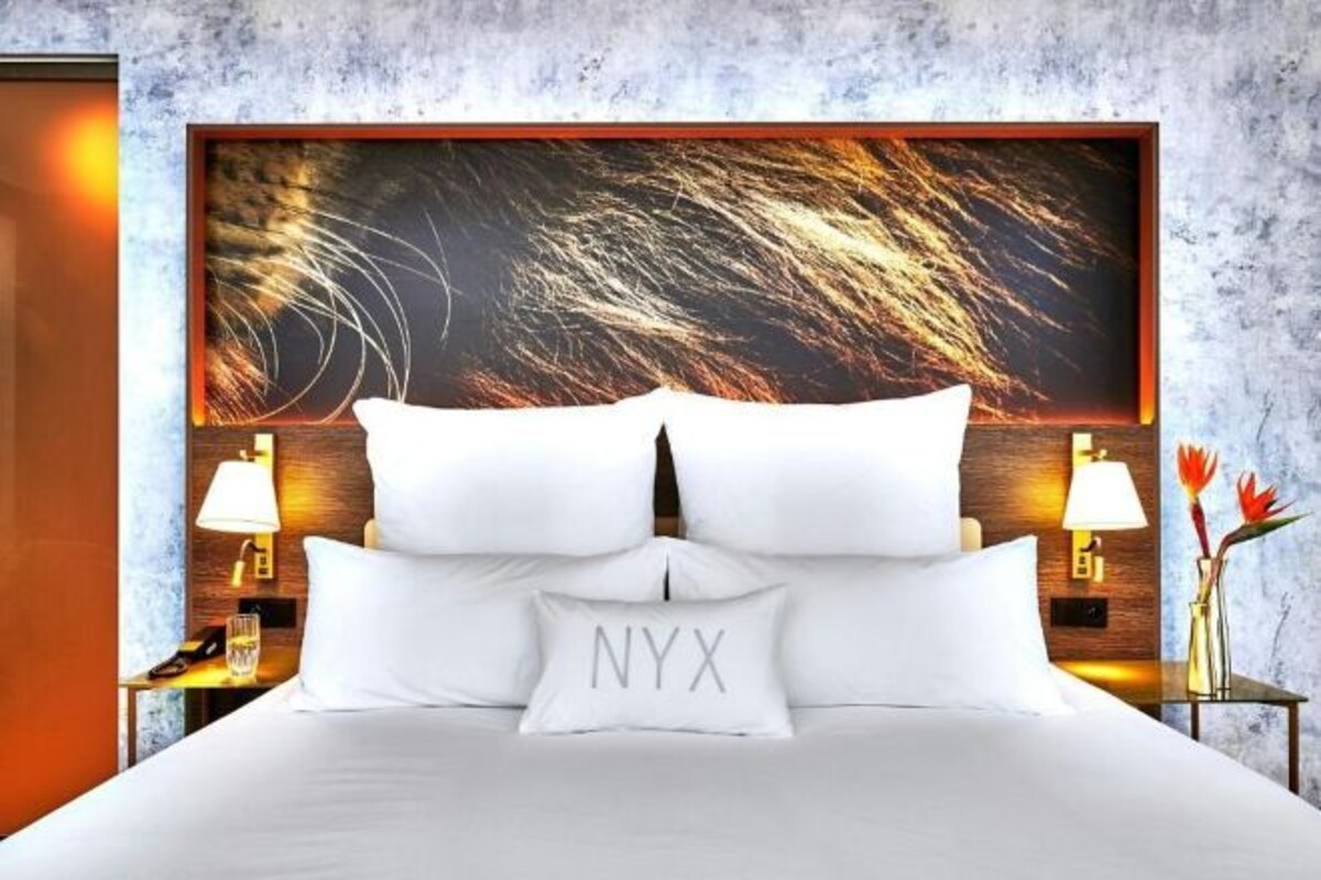 Habitación de hotel con una cama grande, dos lámparas de noche, una mesita de noche y una obra de arte colgada en la pared.