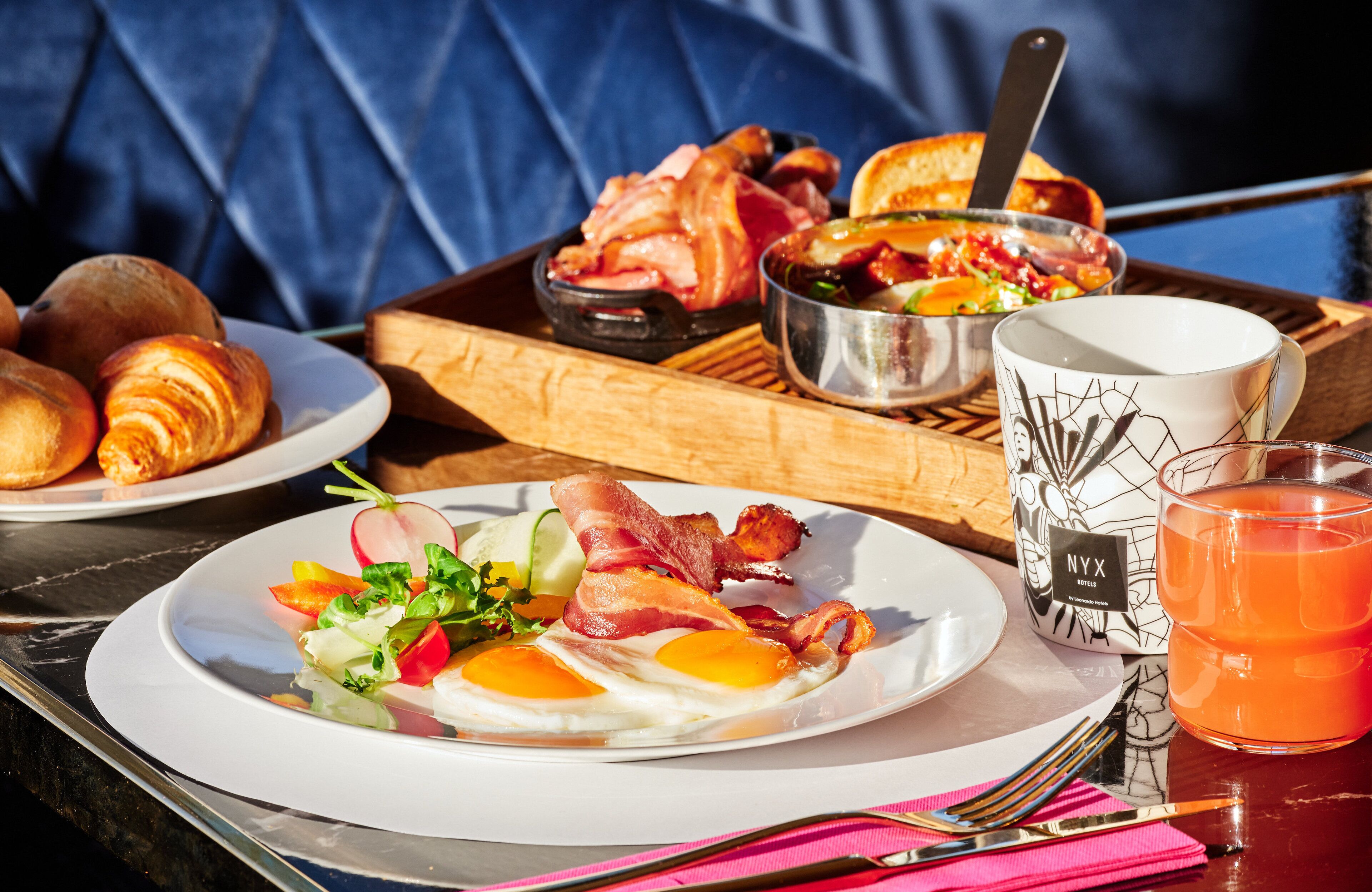 A breakfast setting with croissants, eggs, bacon, and a salad on a tray.