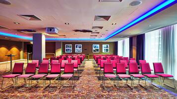 A conference room with rows of red chairs, a patterned carpet, and ceiling lights.