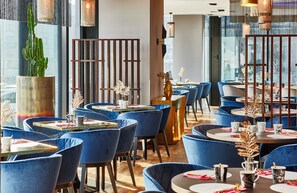 Un restaurante con sillas de terciopelo azul, mesas redondas y una planta de cactus.
