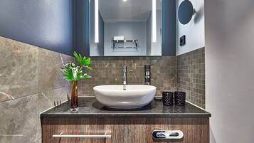 A modern bathroom with a large sink, dark wood vanity, marble tiles, and a small plant.