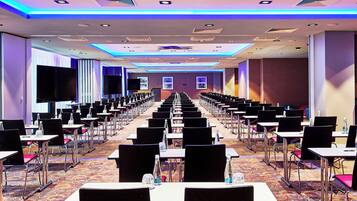 Una sala conferenze con file di tavoli e sedie, grandi schermi e pavimento con tappeto.