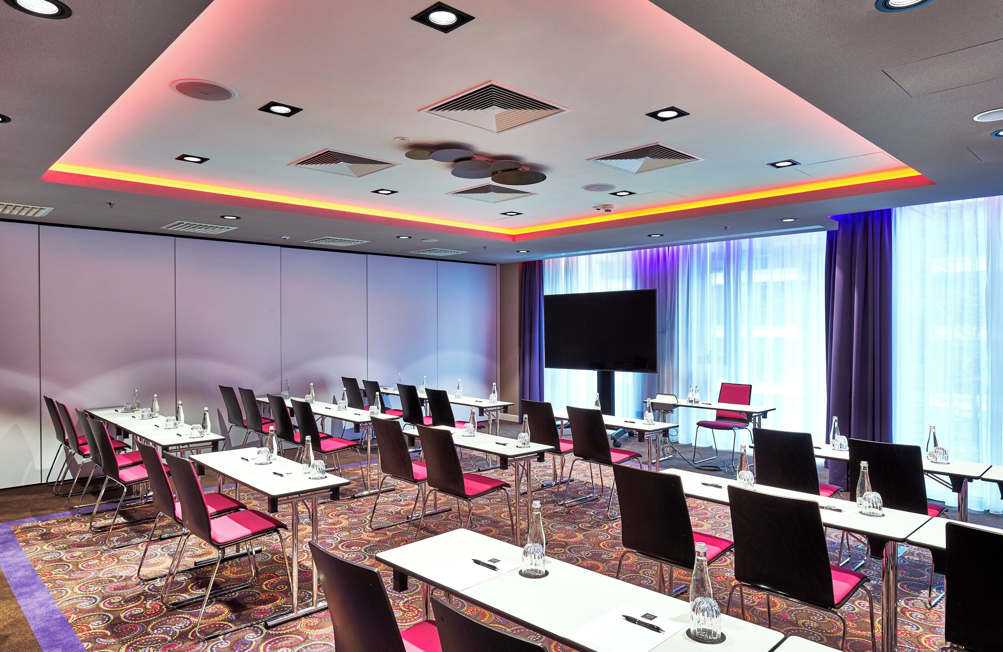 Una sala conferenze con tavoli e sedie, un grande schermo e un tappeto decorato.