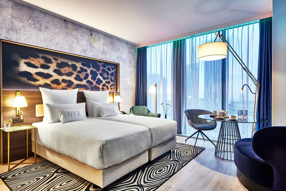 A modern hotel room with a large bed, a desk, and a view of the city.