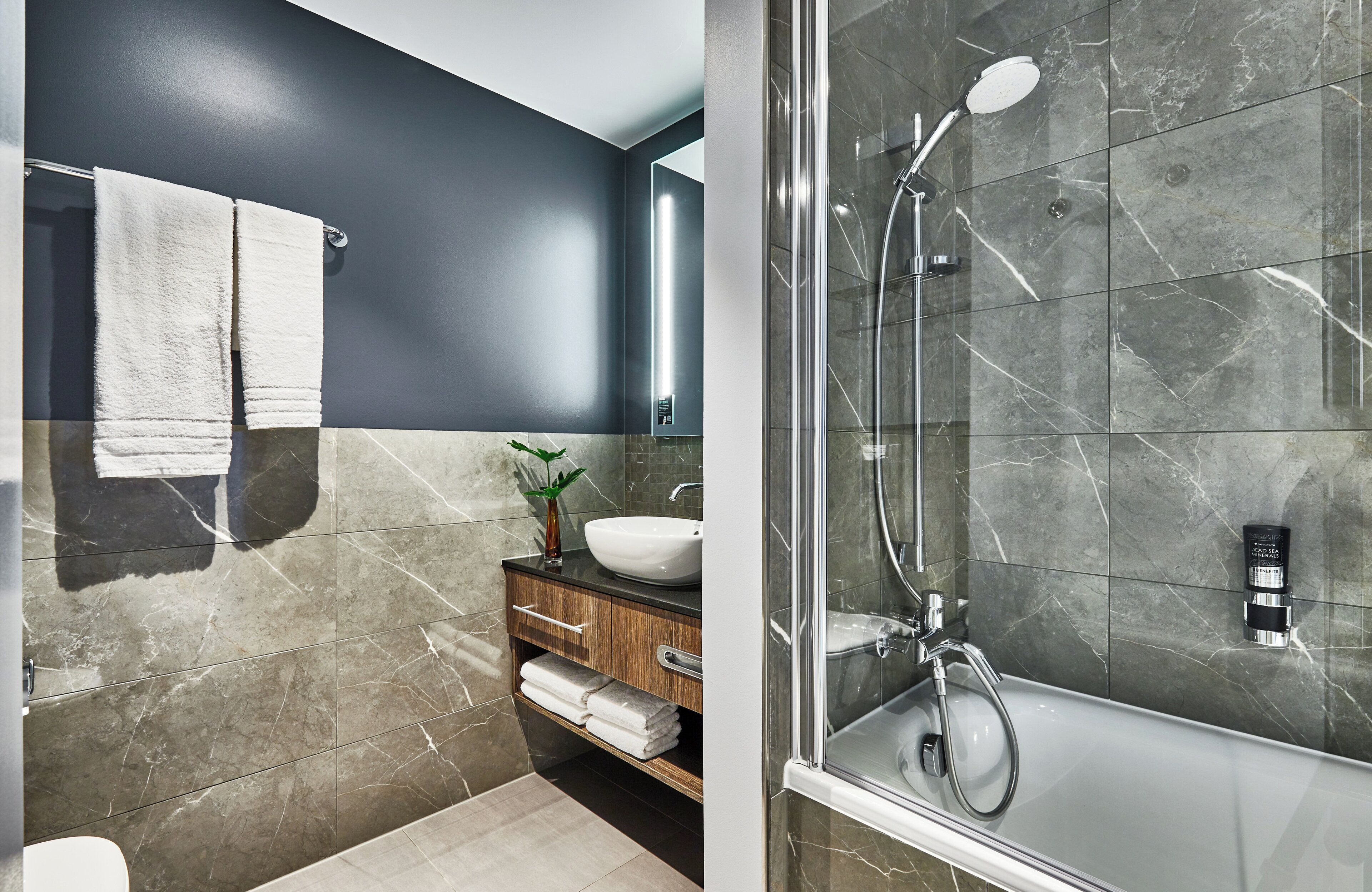 A modern bathroom with a dark wall, a white sink, and a glass-enclosed shower.