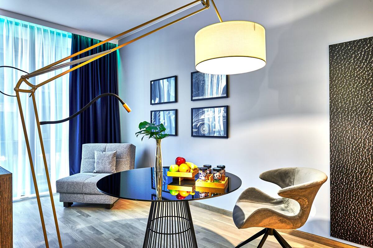 A modern living room with a round glass table, a sofa, a floor lamp, and framed artwork on the wall.