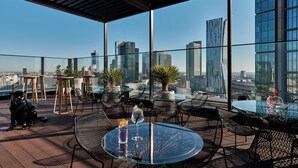 A rooftop terrace with glass tables and chairs, potted plants, and a city skyline view. - NYX Hotel Warsaw by Leonardo Hotels (Warsaw)