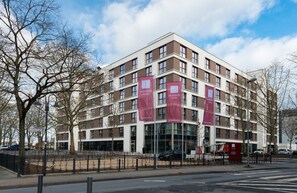 A modern hotel building with multiple floors, large windows, and red banners. - Leonardo Hotel Offenbach Frankfurt (Offenbach am Main)