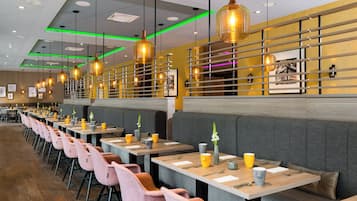 Interior de restaurante moderno com mesas compridas, cabines estofadas e iluminação pendente.