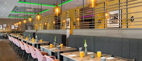 Un intérieur de restaurant moderne, avec de longues tables, des banquettes confortables et des luminaires suspendus.
