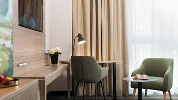 Ein Hotelzimmer mit Schreibtisch, Stuhl, einem kleinen Tisch mit Tasse und Untertasse, einer Lampe und einem an der Wand montierten Fernseher.