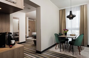 A hotel room with a dining area, a coffee machine, a sofa, a bed, and a window with curtains. - Leonardo Hotel Offenbach Frankfurt (Offenbach am Main)