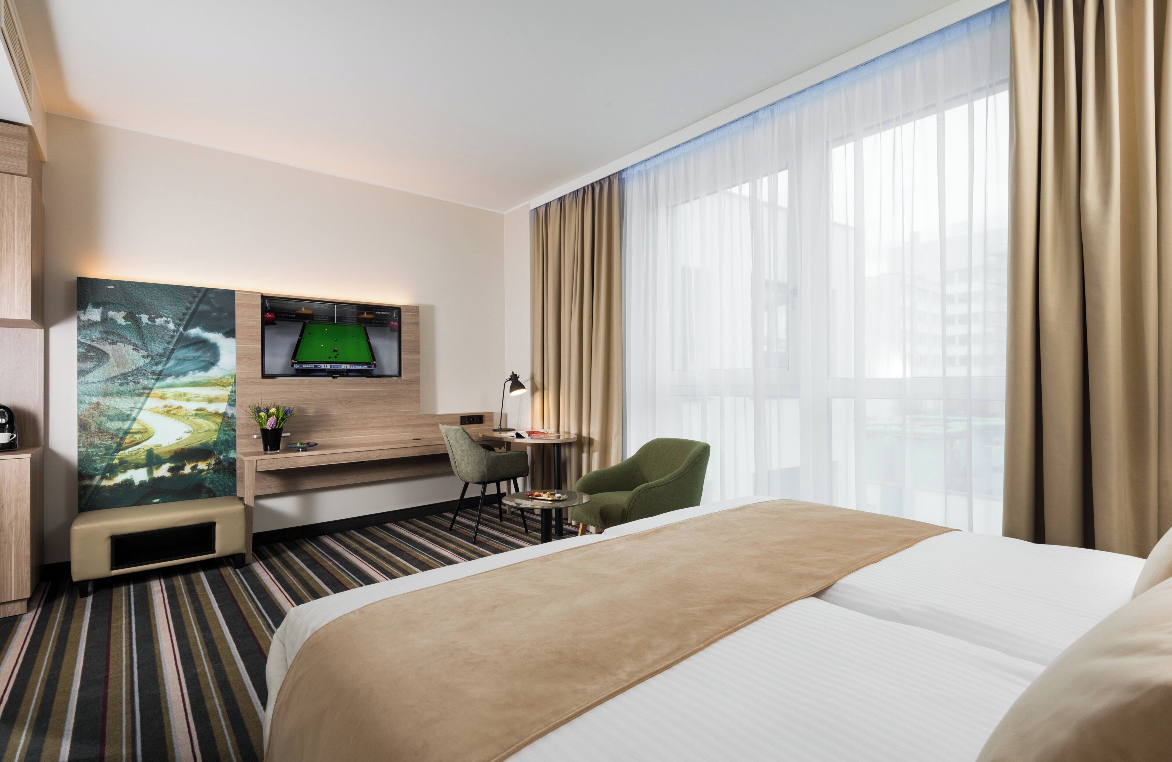 Une chambre d’hôtel avec un lit, un bureau, une chaise, une télévision et une fenêtre avec des rideaux.