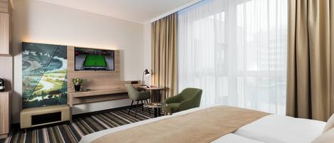 Une chambre d’hôtel avec un lit, un bureau, une chaise, une télévision et une fenêtre avec des rideaux.