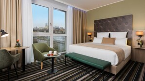 A hotel room with a large bed, a desk with a chair, a small table with a tray of fruit, and a bench. - Leonardo Hotel Offenbach Frankfurt (Offenbach am Main)