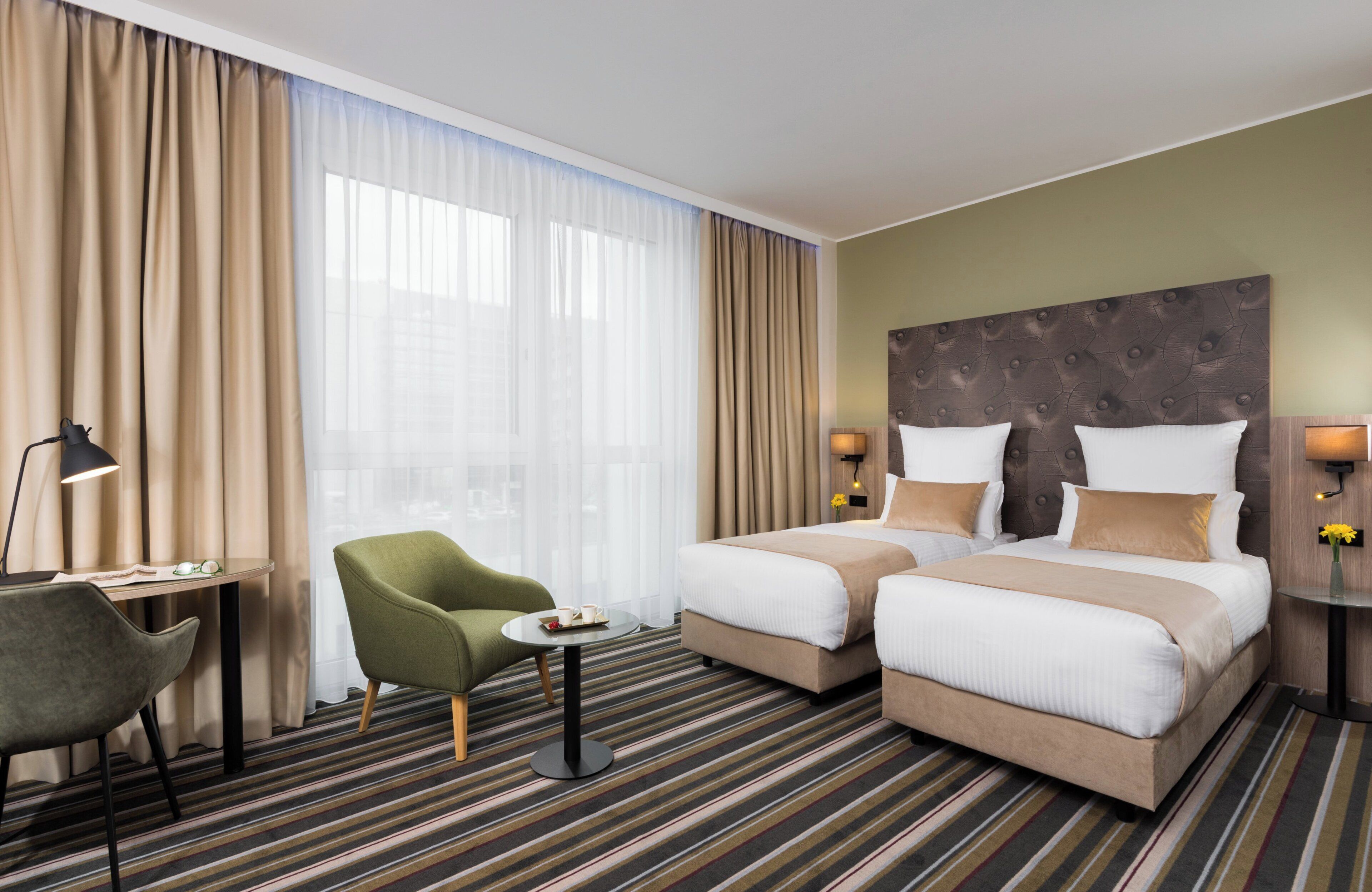 Habitación de hotel con dos camas, un escritorio, una silla y una ventana con cortinas.