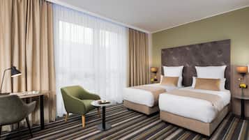 Habitación de hotel con dos camas, un escritorio, una silla y una ventana con cortinas.