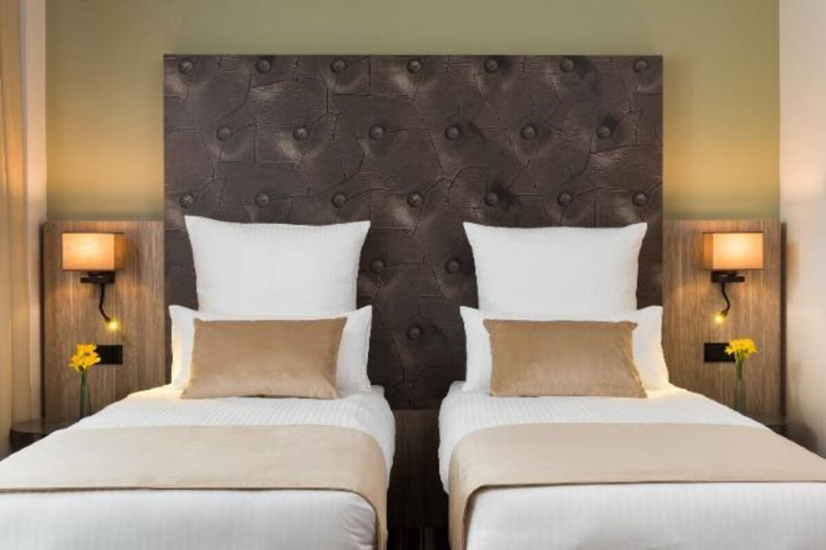 Cama doble con cabecera capitonada, dos mesitas de noche con lámparas y un florero con flores a cada lado.