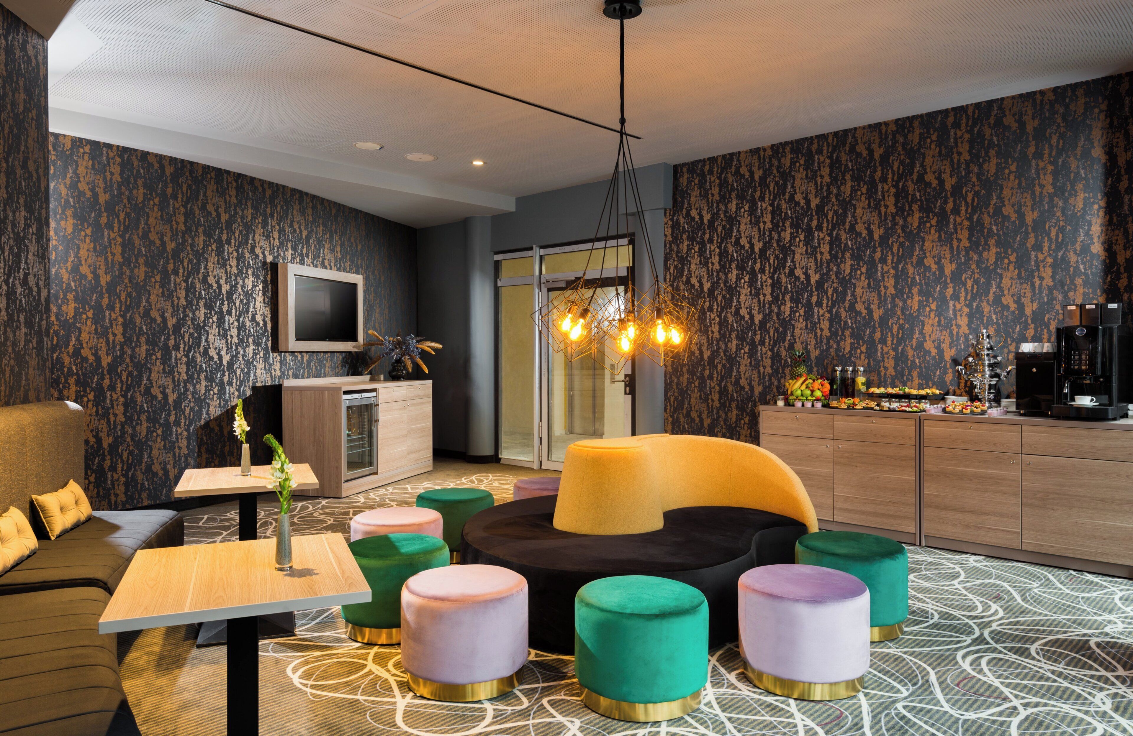 A modern lounge area with a sofa, ottomans, a coffee machine, and a television.