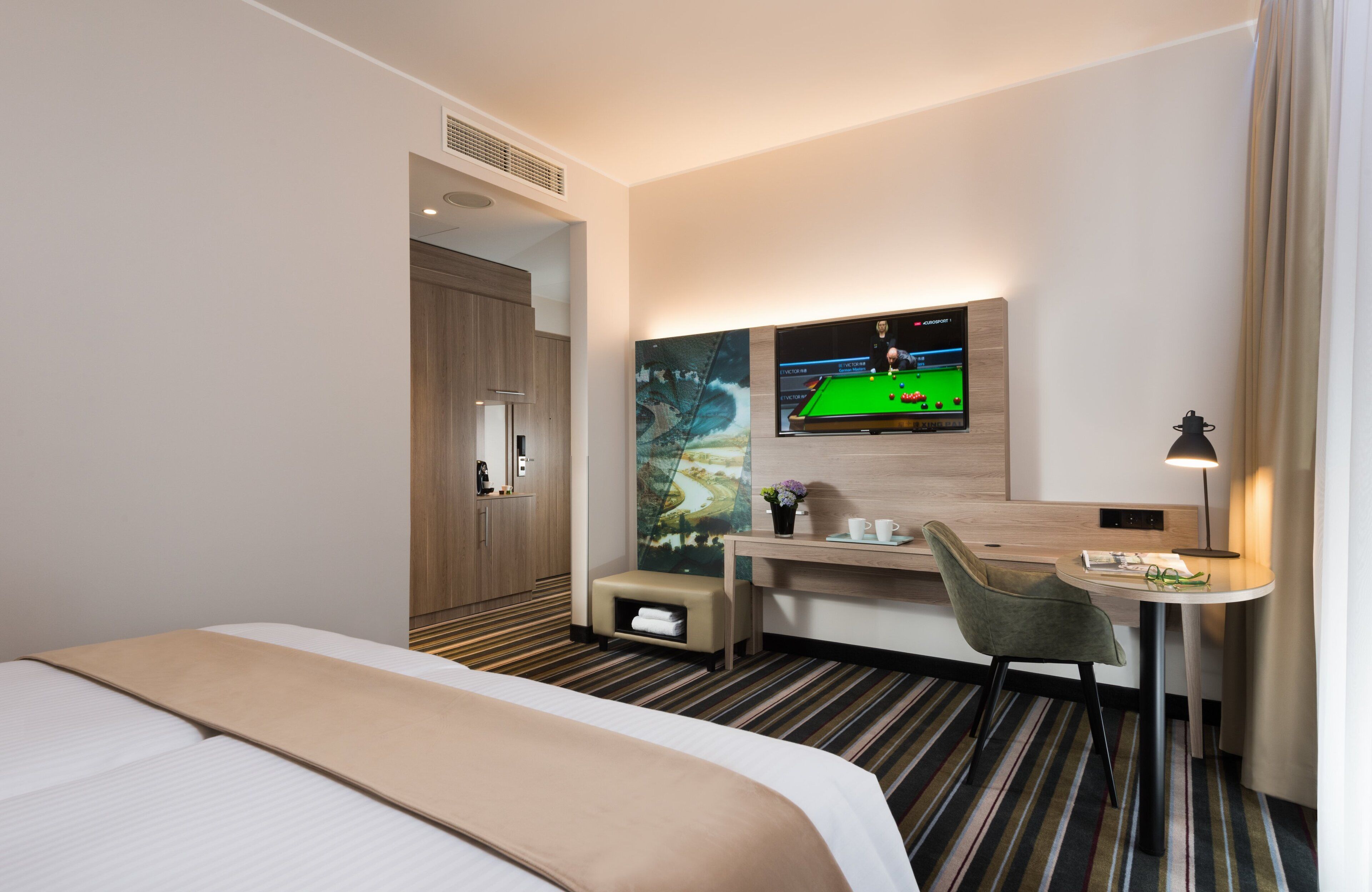Une chambre d’hôtel comprenant un lit, un bureau avec une chaise, une télévision et une petite table avec une lampe.