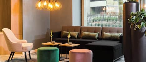 A modern lounge area with a sofa, chairs, ottomans, and a hanging light fixture.