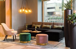 A modern lounge area with a sofa, chairs, ottomans, and a hanging light fixture.