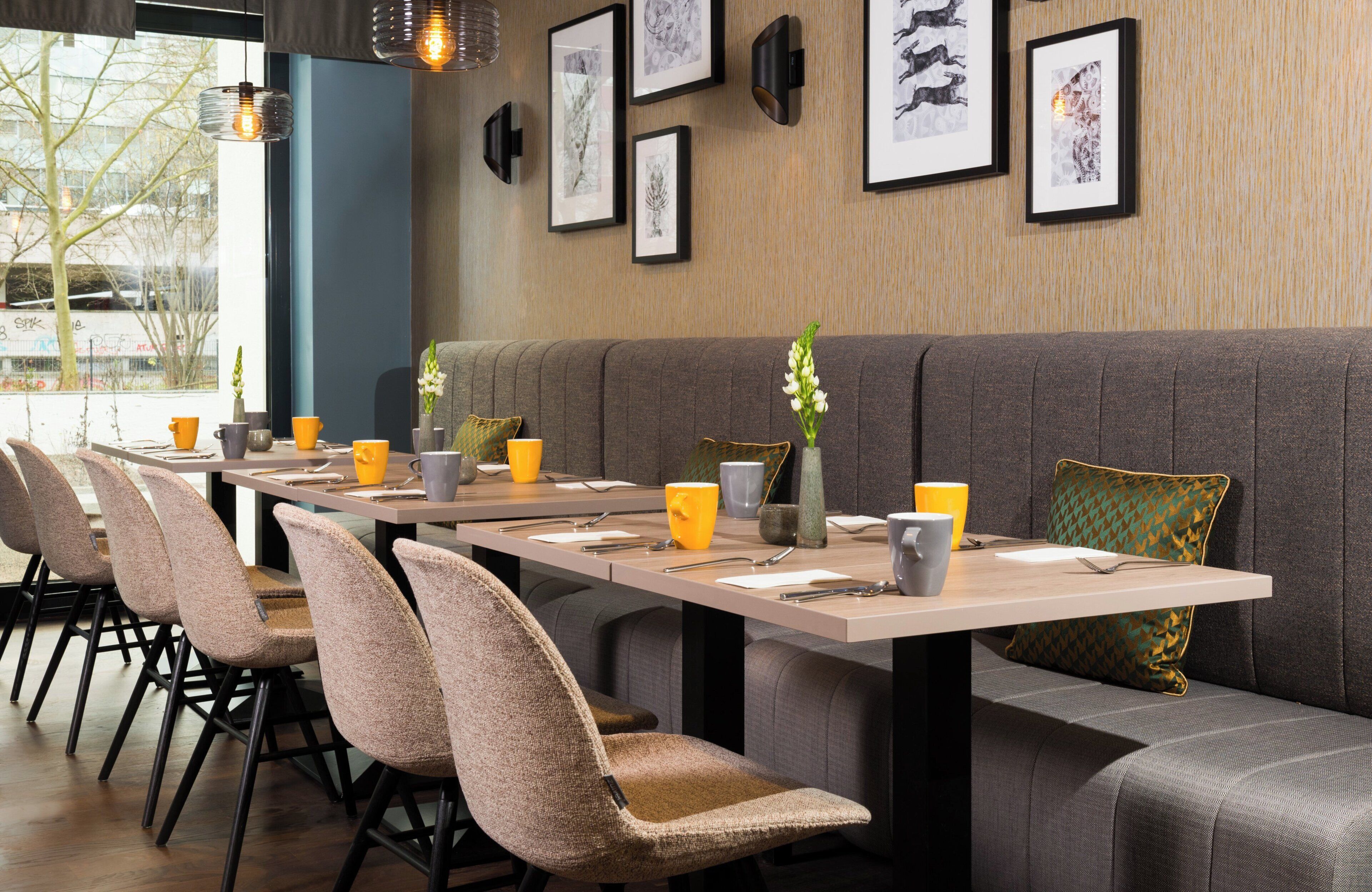 A restaurant with a long table, cushioned chairs, and framed artwork on the wall.