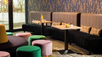Un espace de détente moderne avec un canapé, des poufs colorés, une table avec une bouteille et des verres, et un tapis à motifs.