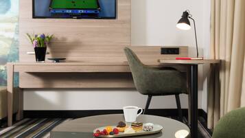 Una habitación de hotel moderna con mesa de billar, un televisor mostrando un partido de billar, un escritorio con lámpara y una pequeña mesa con aperitivos.