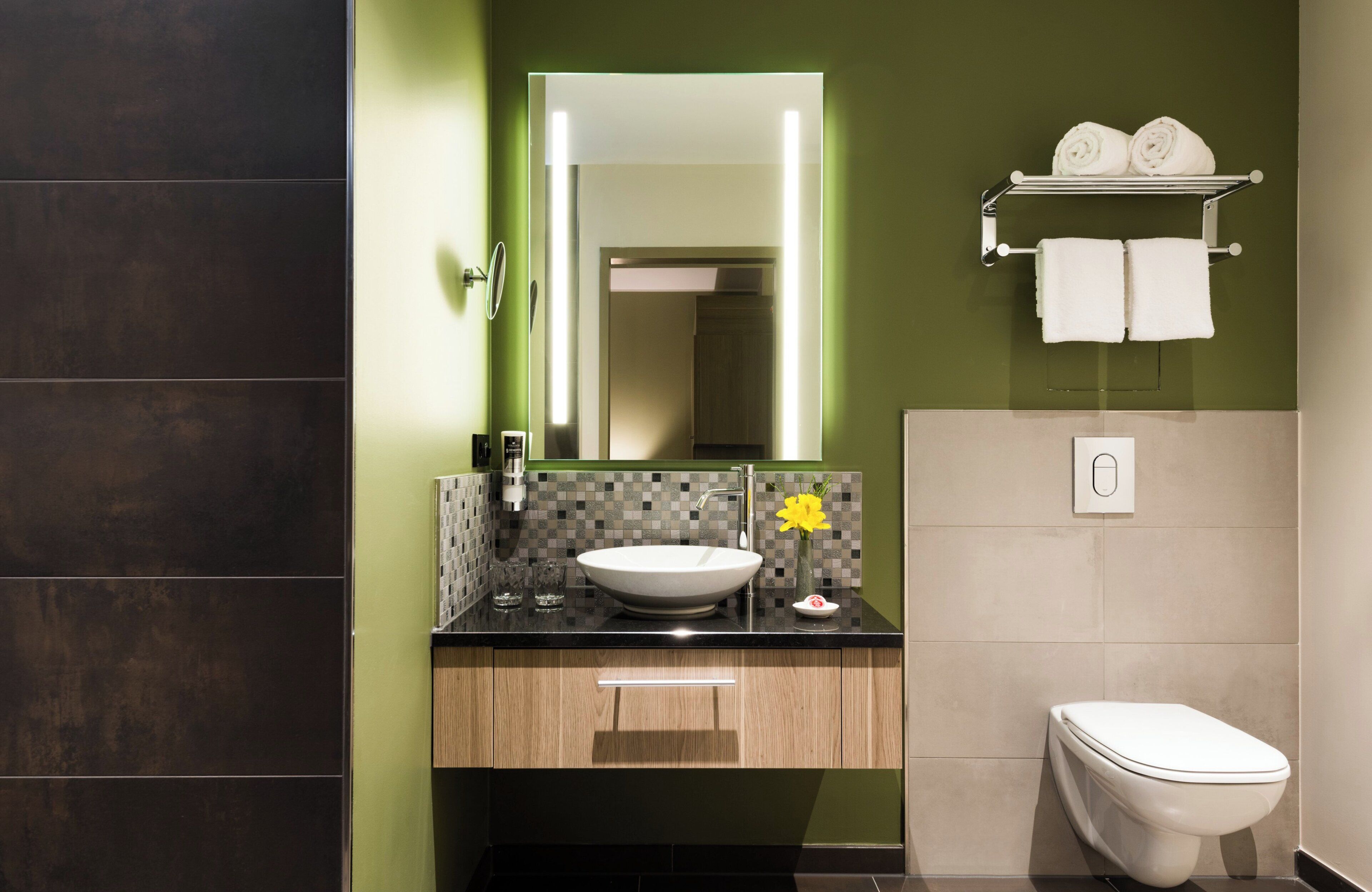 A modern bathroom with a large mirror, a white sink, and a toilet.