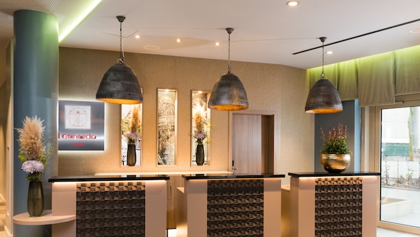 A hotel reception area with a modern design, featuring a reception desk, decorative vases, and pendant lighting. - Leonardo Hotel Offenbach Frankfurt (Offenbach am Main)