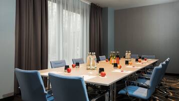 Un salón de conferencias con una larga mesa, sillas azules y vistas al exterior a través de amplias ventanas.