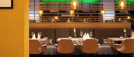 L’intérieur d’un restaurant au design moderne, avec une longue table à manger entourée de chaises, un bar et des luminaires suspendus.