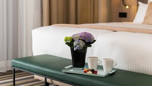 A hotel room with a neatly made bed, a bedside table with a tray of snacks and a cup, and a vase of flowers. - Leonardo Hotel Offenbach Frankfurt (Offenbach am Main)