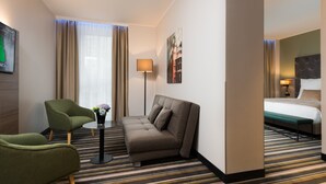 A hotel room with a sofa, armchair, and a small table with a vase of flowers. - Leonardo Hotel Offenbach Frankfurt (Offenbach am Main)