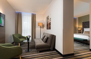Habitación de hotel con sofá, sillón y una pequeña mesa con un jarrón de flores.