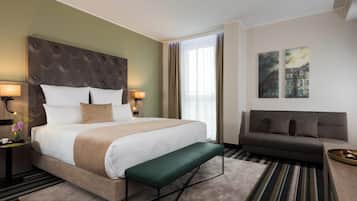 Quarto de hotel com uma cama grande, um banco, um sofá e duas pinturas na parede.