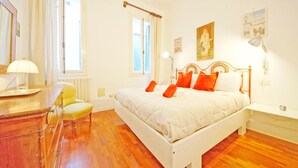 A bedroom with a bed, bedside table, lamp, chair, and a window with curtains. - DolceVita Apartments N. 241 (Venice)